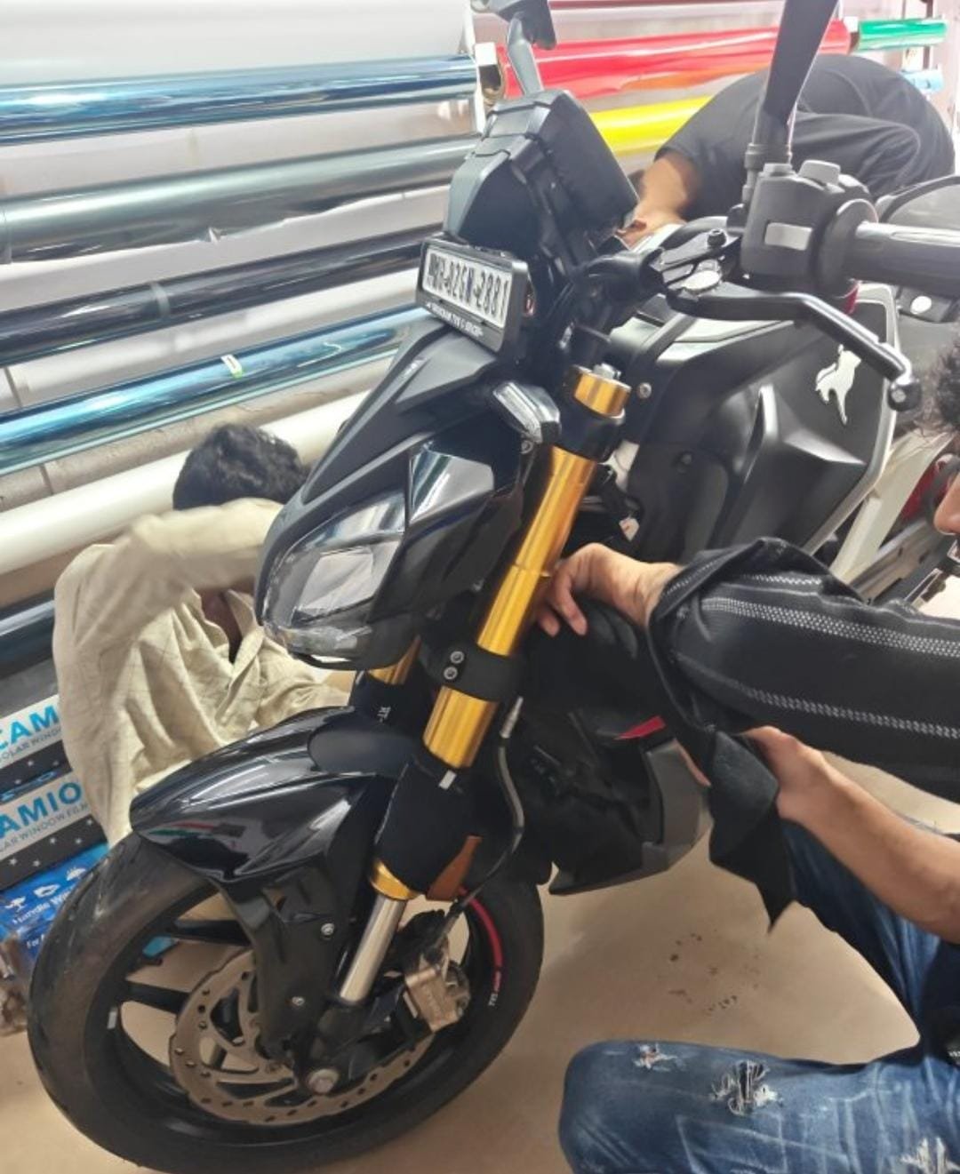 Motorcycle being detailed beside racks of film rolls at M7WRAP