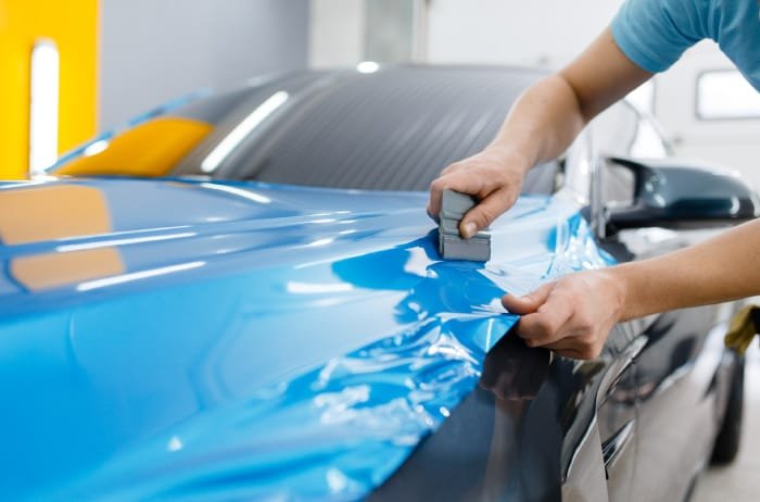 Blue vinyl wrap being squeegeed onto a car bonnet